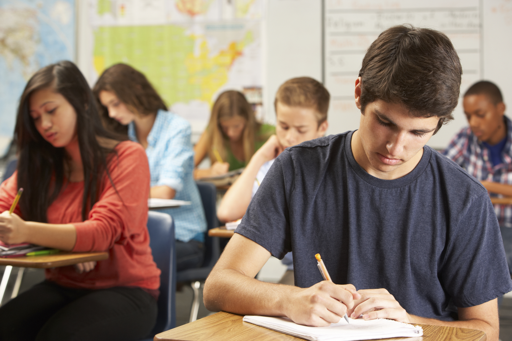 Male student writing in a notebook at a desk in a classroom - Wells ...